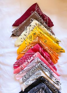 a pile of different colored bandannas laying on top of a white bed sheet