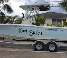 a white and black boat parked in front of a house with palm trees behind it