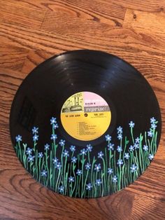 a record with blue flowers painted on it sitting on a wooden table next to a wall