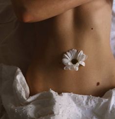 a woman's stomach with a flower pinned to the back of her body in white linens