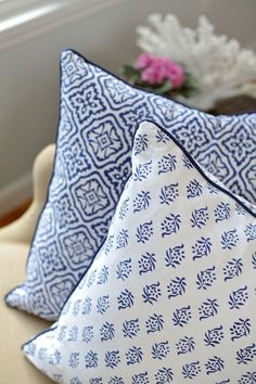 two blue and white pillows sitting on top of a couch next to a window sill