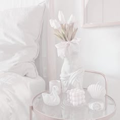 a glass table topped with a vase filled with flowers and seashells next to a bed