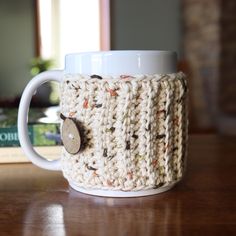 a crocheted coffee cup holder with a button on the side sitting on a table