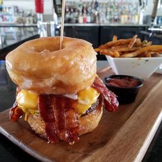 a bacon, egg and cheese breakfast sandwich on a wooden board with fries in the background