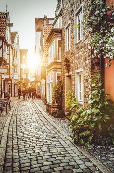 an old cobblestone street with people walking on it and the sun setting in the background