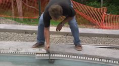 a man bending over to pick up something off the ground next to a swimming pool