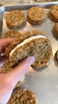 a hand holding an oatmeal sandwich in front of some cookies