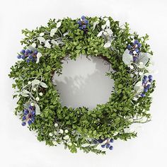 an overhead view of a wreath with blue flowers and greenery on the front, against a white background