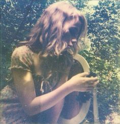 a woman sitting on the ground holding a cell phone in her right hand and looking at it