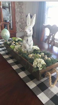 a wooden table topped with an easter centerpiece filled with white flowers and greenery