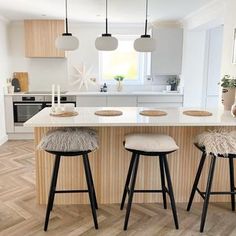 two stools sit at the center of a kitchen island with three lights above it