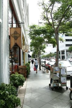 the sidewalk is lined with shops and parked cars