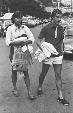 an old photo of two people walking down the street with towels on their laps and bags