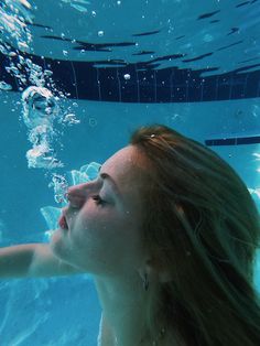 a woman swimming under water with her head above the water's surface, looking up into the air