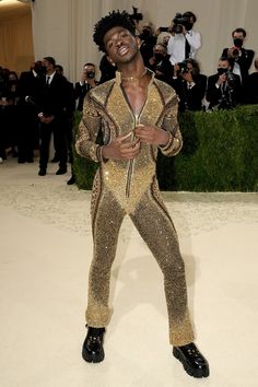 a man in gold and black outfit standing on a white carpet with people taking pictures behind him