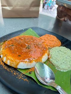 a black plate topped with food on top of a green napkin next to a spoon