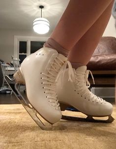 the legs and feet of a person wearing ice skates in a room with wood flooring