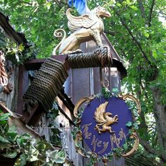 a blue sign hanging from the side of a wooden building next to green leaves and trees