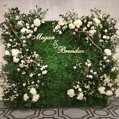 a green wall with white flowers and greenery in the shape of a heart on it