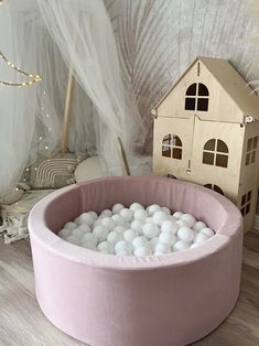 a pink round bed with white balls in it and a doll house on the floor