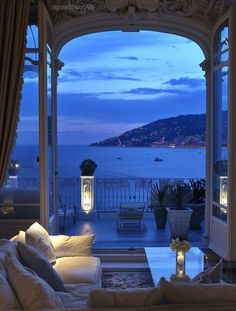 a living room filled with furniture next to a large window overlooking the ocean at night