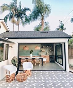 an open garage door with wicker chairs and tables in the front yard, surrounded by palm trees