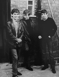 three young men standing next to each other in front of a brick wall and door