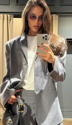 a woman taking a selfie with her cell phone while wearing a gray suit and heels