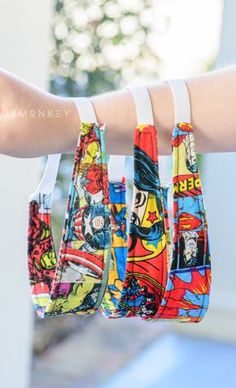 a person's hand holding three small purses with comic covers on them and white wristbands