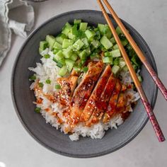 a bowl filled with rice, meat and cucumbers next to chopsticks