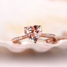 an engagement ring with a heart shaped morganite in the center on a white shell