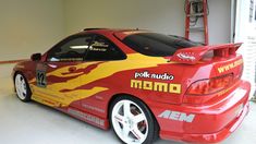 a red car with yellow flames painted on it's side parked in a garage