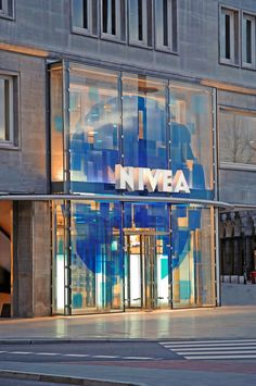 the entrance to an office building that is lit up with blue and white glass panels