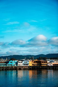 there are many houses on the water by the dock with boats in the harbor and clouds in the sky