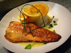 a white plate topped with fish and rice next to an orange on top of a table