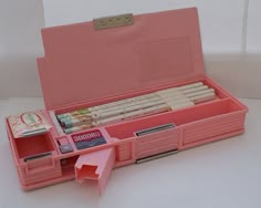 an open pink box containing several different types of pens and pencils on a white surface