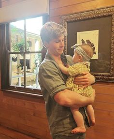 a man holding a baby in his arms near a window with a bird on it