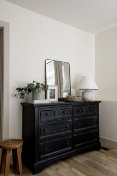 a black dresser with a mirror, lamp and plant on it in a white room