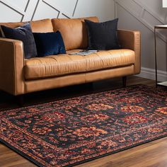 a brown leather couch sitting on top of a wooden floor next to a black rug