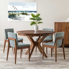 a dining room table with four chairs and a vase on the top, in front of a painting