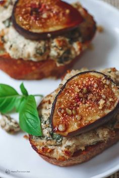 two stuffed eggplant sandwiches are on a white plate with basil leaves and cheese