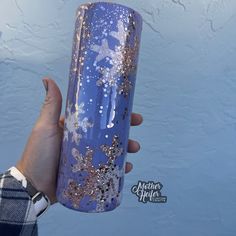 a person holding up a purple and gold glittered tumbler with snowflakes on it