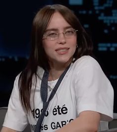 a woman with glasses sitting in front of a tv screen wearing a white t - shirt