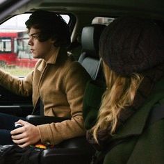 two people sitting in the driver's seat of a car, one holding a steering wheel