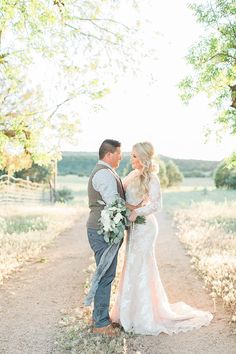 a bride and groom standing in the middle of a dirt road