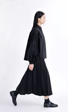 a woman in black is walking down the street wearing a long dress with pleated sleeves