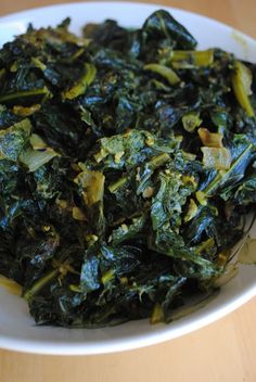 a white bowl filled with cooked greens on top of a wooden table next to a fork