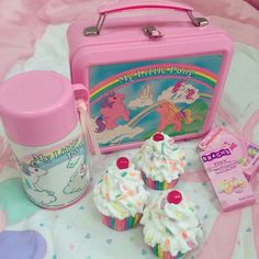 a pink lunchbox, cupcakes and other items on a bed