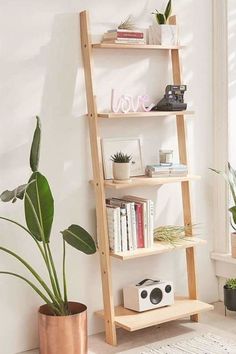 a wooden ladder shelf with books and plants on it in front of a white wall