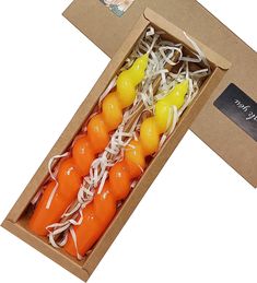 four orange and yellow candles in a cardboard box